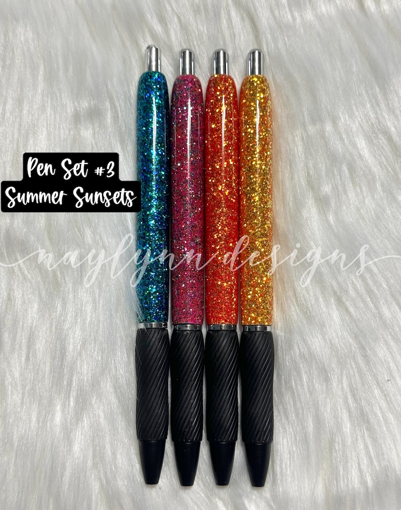 May include: Set of four glitter pens with black ink. The pens have a black grip and silver accents. The glitter colors are teal, pink, orange, and yellow. The text "Pen Set #3 Summer Sunsets" is visible in the image.