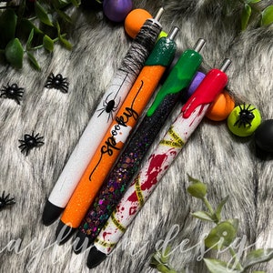 May include: Four Halloween themed pens with different designs. One pen is white with orange glitter and black spider and the text "spooky". Another pen is black with green glitter and dripping green slime. The third pen is white with black glitter and dripping red slime with a yellow and black caution tape design. The fourth pen is orange with black glitter and a spider web design.