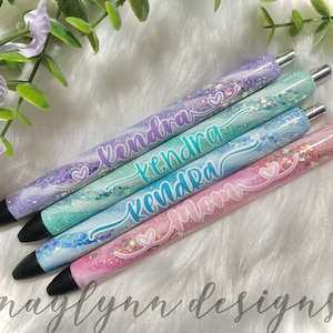 May include: Four personalized pens with glitter and marble designs. The pens are labeled "Kendra", "Mom", and two more "Kendra" names.
