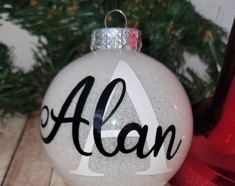 Può includere: Addobbo natalizio bianco con glitter con il nome "Alan" scritto in lettere corsive nere.