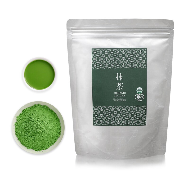 May include: A silver pouch with a green label that says "抹茶 ORGANIC MATCHA" and has a green and white pattern. The pouch contains green matcha powder. There is a small white bowl with green matcha powder and a small white bowl with green matcha tea.