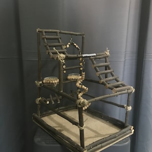 Peut inclure: Une structure de jeu en bois faite à la main pour oiseaux ou petits animaux. Elle comprend plusieurs niveaux, des échelles et des plateformes, construits à partir de branches et de ficelle. La structure comprend de petits bols et des décorations en bois suspendues.