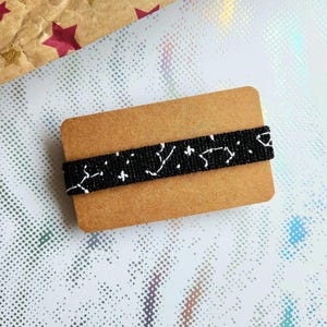 May include: A black and white beaded bracelet with a star pattern on a brown card.