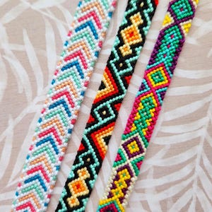 May include: Three colorful friendship bracelets with geometric patterns. The bracelets are made with colorful embroidery floss and feature a variety of colors, including pink, blue, green, yellow, orange, and black.