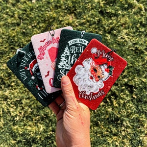 May include: Four Christmas-themed car air fresheners. The air fresheners are red, green, and pink with white text. The text on the air fresheners reads "I like them real, the s...