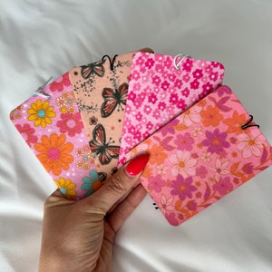 May include: Five pink and orange floral patterned fabric air fresheners with a white string hanging from each. The air fresheners are held in a hand with red nail polish.