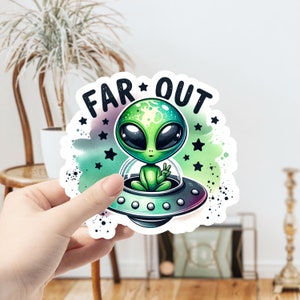 May include: A green alien with a peace sign sits in a flying saucer with the words "FAR OUT" above it. The background is a watercolor wash of green, purple, and blue with white stars.