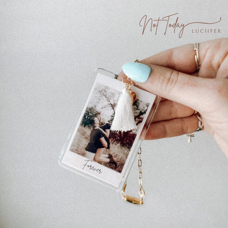 May include: Clear acrylic keychain with a photo of a couple, a white tassel, and gold-coloured hardware. The photo has the word "Forever" printed on it. The keychain also has the words "Not Today" and "LUCIIFER" printed on it.