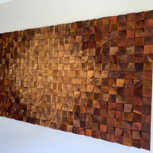Puede incluir: Una pieza de arte de pared hecha de madera con un patrón ondulado. La madera es de color marrón oscuro y tiene un aspecto natural y rústico. La pieza está compuesta por muchos cuadrados pequeños de madera que están dispuestos en un patrón escalonado.