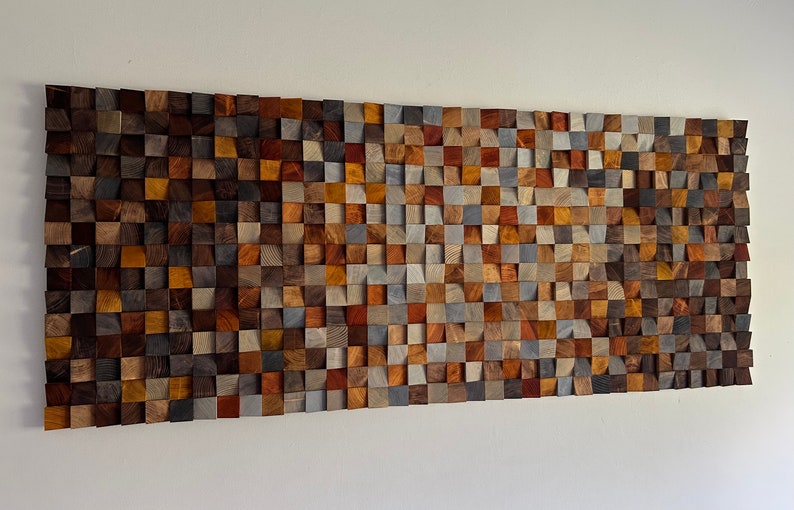 K&ouml;nnte beinhalten: Ein Wandkunstwerk aus Holz mit einem Mosaik aus verschiedenen farbigen Holzquadraten. Die Quadrate sind in einem Muster angeordnet, das einen wellenartigen Effekt erzeugt. Das Holz ist eine Mischung aus braunen, grauen und roten T&ouml;nen.