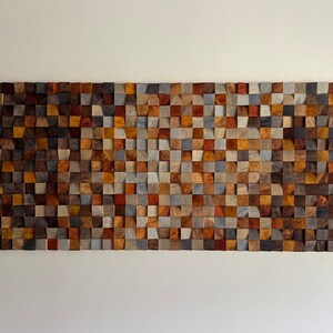 K&ouml;nnte beinhalten: Ein Wandkunstwerk aus kleinen, quadratischen Holzbl&ouml;cken in verschiedenen Braunt&ouml;nen, Graut&ouml;nen und Beige. Die Bl&ouml;cke sind in einem geometrischen Muster angeordnet und schaffen ein strukturiertes und visuell interessantes Design.