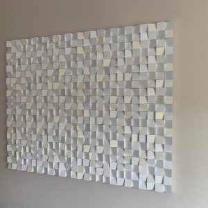 May include: A white wall art piece made of many small, square, 3D tiles. The tiles are arranged in a pattern and create a textured effect.