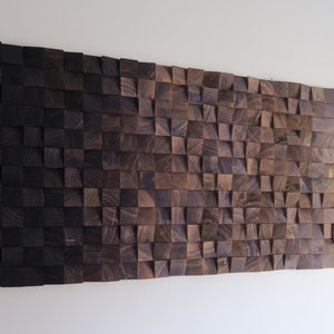 Puede incluir: Una pieza de arte de pared hecha de cuadrados de madera oscura dispuestos en un patrón de onda. Los cuadrados son de diferentes tamaños y tienen una veta de madera natural.