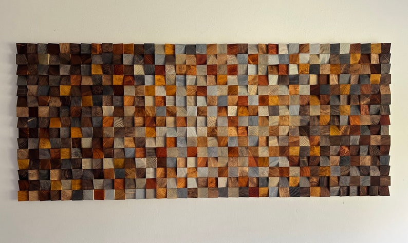 K&ouml;nnte beinhalten: Ein Wandkunstwerk aus Holzbl&ouml;cken in verschiedenen Braunt&ouml;nen, Graut&ouml;nen und Blaut&ouml;nen. Die Bl&ouml;cke sind in einem geometrischen Muster angeordnet und schaffen ein modernes und abstraktes Design.