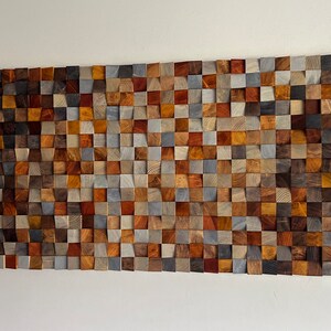 K&ouml;nnte beinhalten: Ein Wandkunstwerk aus Holzbl&ouml;cken in verschiedenen Braunt&ouml;nen, Graut&ouml;nen und Blaut&ouml;nen. Die Bl&ouml;cke sind in Wellenform angeordnet und schaffen ein einzigartiges und modernes Design.