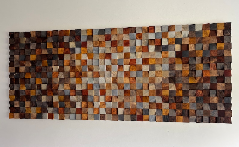 K&ouml;nnte beinhalten: Ein Wandkunstwerk aus Holzbl&ouml;cken in verschiedenen Braunt&ouml;nen, Graut&ouml;nen und Blaut&ouml;nen. Die Bl&ouml;cke sind in Wellenform angeordnet und schaffen ein einzigartiges und modernes Design.