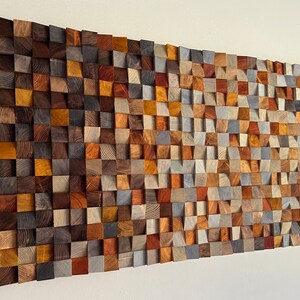 K&ouml;nnte beinhalten: Ein Wandkunstwerk aus Holz mit einem Wellenmuster. Das Holz ist in verschiedenen Farben, darunter Braun, Grau und Orange. Das Holz ist in einem Gittermuster angeordnet.