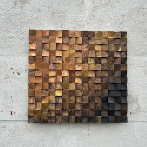 May include: A wall art piece made of wood with a gradient of brown shades. The wood is arranged in a grid pattern, with each piece slightly raised from the next. The piece is mounted on a grey wall.