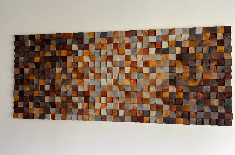 K&ouml;nnte beinhalten: Ein Wandkunstwerk aus Holzquadraten in verschiedenen Braunt&ouml;nen, Graut&ouml;nen und Beiget&ouml;nen. Die Quadrate sind in Wellenform angeordnet und schaffen ein einzigartiges und modernes Design.