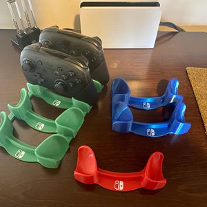 May include: Three green, two blue, and one red plastic stands for holding Nintendo Switch controllers. The stands have the Nintendo Switch logo printed on them.