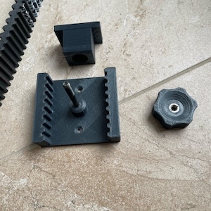 May include: A black 3D printed gear rack with a black gear and a black knob. The gear rack has a metal rod sticking out of the top.