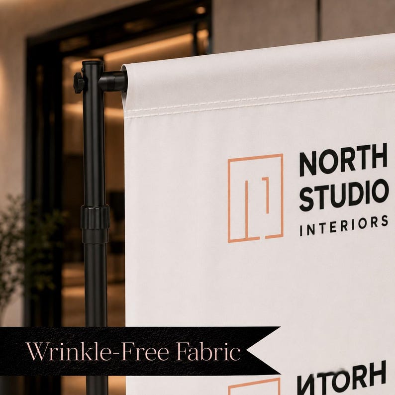 May include: A white fabric banner suspended on a black metal stand. The banner features a peach-colored geometric logo and the black text "NORTH STUDIO INTERIORS". A black banner overlay at the bottom displays the text "Wrinkle-Free Fabric".