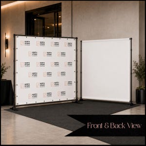 May include: A black metal adjustable banner stand frame featuring a white backdrop with a repeating North Studio Interiors logo in black and orange text. A second plain white banner is positioned to the right, showing the front and back view.