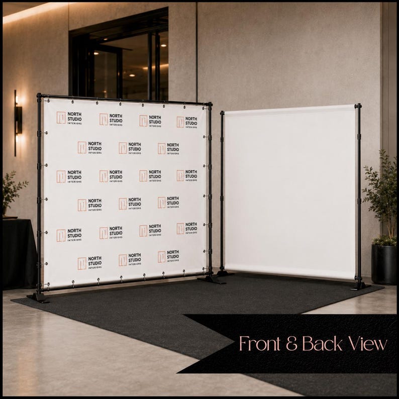 May include: A black metal adjustable banner stand frame featuring a white backdrop with a repeating North Studio Interiors logo in black and orange text. A second plain white banner is positioned to the right, showing the front and back view.