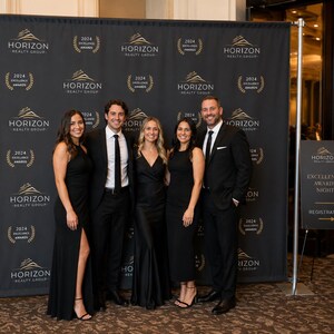 May include: A black step and repeat backdrop featuring the gold Horizon Realty Group logo and 2024 Excellence Awards text in a repeating pattern. A separate black sign on a stand displays Horizon Realty Group Excellence Awards Night Registration.