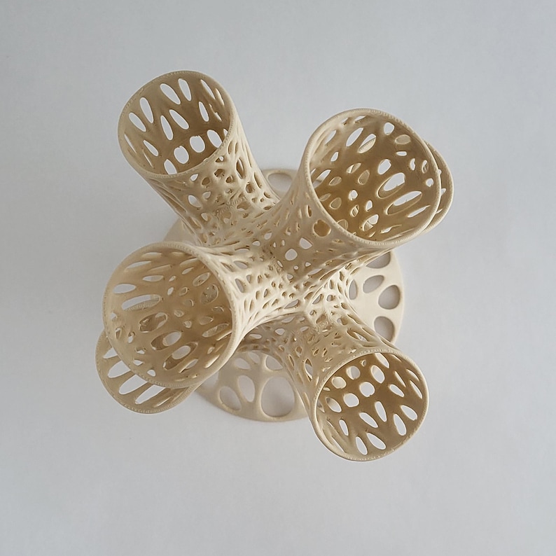 Puede incluir: Un jarr&oacute;n de cer&aacute;mica beige con un dise&ntilde;o &uacute;nico, intrincado y calado. El jarr&oacute;n tiene cuatro aberturas y una base circular.