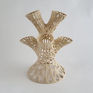 Puede incluir: Un jarr&oacute;n de cer&aacute;mica de color crema con un dise&ntilde;o &uacute;nico, intrincado y calado. El jarr&oacute;n tiene cinco aberturas, cada una con una forma acampanada en forma de trompeta. El jarr&oacute;n es perfecto para exhibir flores u otros art&iacute;culos decorativos.
