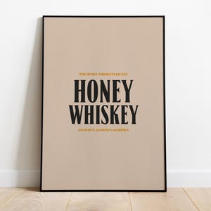 May include: A beige poster with a black frame. The poster has the text "The Honey Whiskey Kickin' Honey Whiskey Go Down, Go Down, Go Down" in black and gold text.