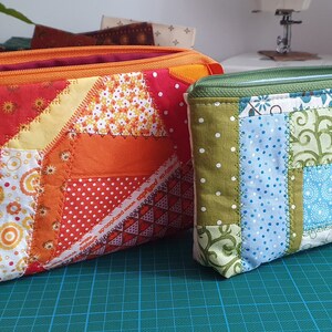 Op de afbeelding: Twee ritsvakjes van patchwork stof. De grotere tas is oranje, rood en geel. De kleinere tas is groen, blauw en wit.
