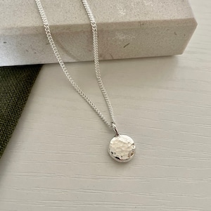 May include: A silver chain necklace with a hammered silver circle pendant.