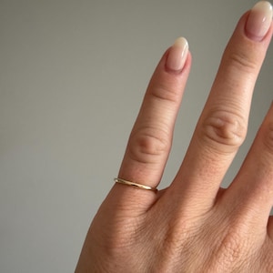 Pode incluir: Um anel de banda fina em ouro polido com uma superf&iacute;cie lisa e arredondada. O anel apresenta um design circular simples e cont&iacute;nuo com um acabamento met&aacute;lico reflexivo, usado num dedo para demonstrar o seu perfil fino e aspeto cl&aacute;ssico.