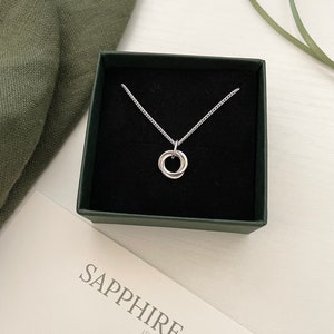 May include: A silver necklace with a simple, twisted circle pendant in a black box with a green lid. The box has a white label with the text "Sapphire & Rose Jewellery".