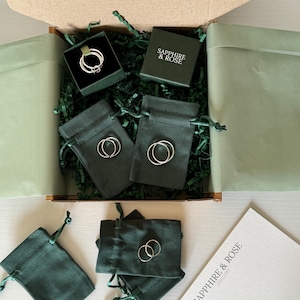 May include: A cardboard shipping box containing dark green velvet jewellery pouches and a small square box with the text SAPPHIRE & ROSE. Inside are several thin silver rings, some placed on the pouches and others inside the box. A white card with the text SAPPHIRE & ROSE JEWELLERY is included.