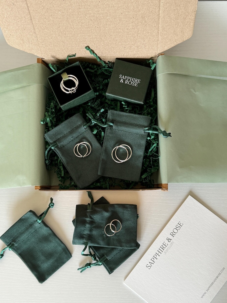 May include: A cardboard shipping box containing dark green velvet jewellery pouches and a small square box with the text SAPPHIRE & ROSE. Inside are several thin silver rings, some placed on the pouches and others inside the box. A white card with the text SAPPHIRE & ROSE JEWELLERY is included.