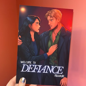 May include: A print featuring a couple in a dramatic pose, with the text "WELCOME TO DEFIANCE MISSOURI" in white. The artwork has a dark, moody color palette with the couple in the foreground.