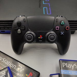 Peut inclure: Une console PlayStation 2 noire avec une manette DualSense noire, deux boîtiers de jeux PlayStation 2 et deux disques de jeux PlayStation 2. Les boîtiers de jeux sont bleus et noirs avec le texte "PlayStation 2" et "Playstation" dessus. Les disques de jeux sont argentés avec un design bleu et noir.