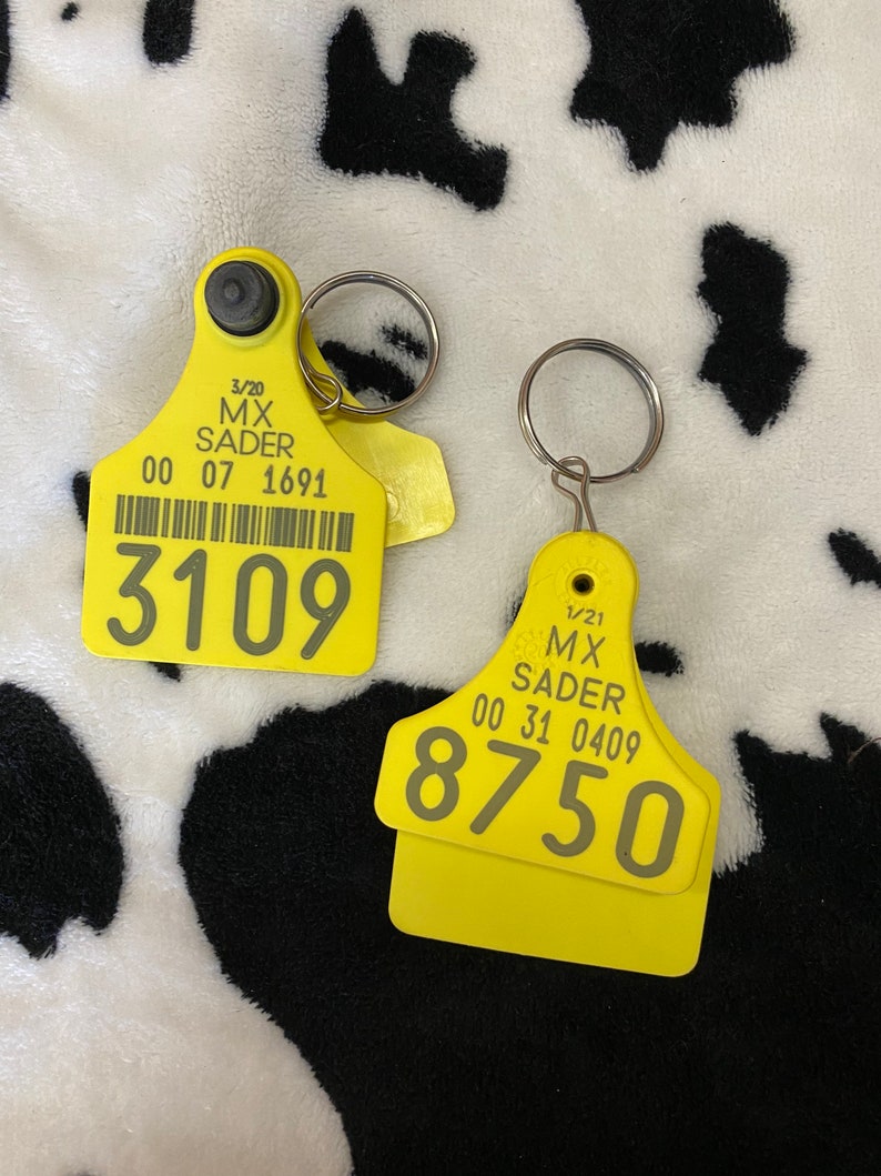 May include: Two yellow livestock ear tags with silver key rings. One tag displays the number 3109, the other displays 8750. Both tags have printed text including the name "MX SADER" and a date.
