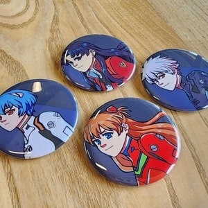 May include: Four round button pins featuring anime characters. The pins are on a wooden surface. The characters are from the anime series Neon Genesis Evangelion. The characters are Asuka Langley Soryu, Rei Ayanami, Shinji Ikari, and Misato Katsuragi.
