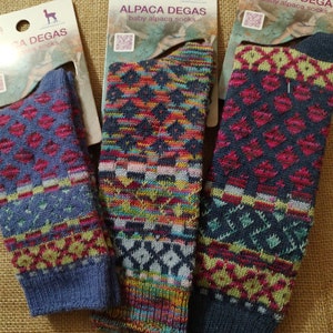 May include: Three pairs of baby alpaca socks in different colors and patterns. The socks are made of soft, warm alpaca wool and are perfect for keeping little feet cozy. The socks are labeled "Alpaca Degas" and feature a small alpaca logo.