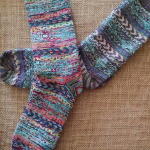 May include: A pair of colorful knitted socks with a mix of blue, pink, and green hues. The socks feature a patterned design with horizontal stripes and geometric accents. The socks are made of a soft, textured material.