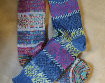 May include: Two pairs of colorful knitted socks. One pair features a patchwork design with geometric patterns in blue, pink, yellow, and white. The other pair has a blue base with pink and yellow accents. The socks are made of a soft, textured material.