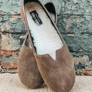 K&ouml;nnte beinhalten: Ein Paar braune Slipper aus Wildleder mit einem wei&szlig;en Kunstfellfutter. Die Schuhe haben ein Etikett mit der Aufschrift "DO NOT  CONSUME  HABBOCHOCO".