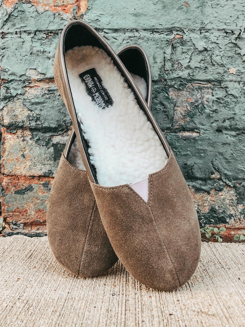 K&ouml;nnte beinhalten: Ein Paar braune Slipper aus Wildleder mit einem wei&szlig;en Kunstfellfutter. Die Schuhe haben ein Etikett mit der Aufschrift "DO NOT  CONSUME  HABBOCHOCO".