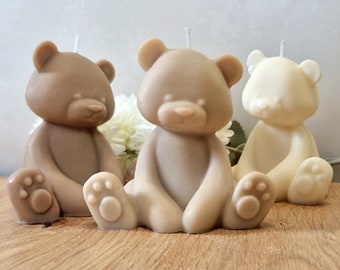 Pode incluir: Três velas em forma de urso de peluche em bege, castanho e branco. As velas estão sobre uma superfície de madeira.