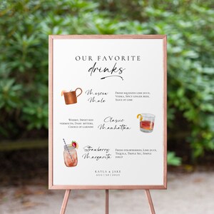 May include: A white sign with a wooden frame lists three cocktails: Moscow Mule, Classic Manhattan, and Strawberry Margarita. Each cocktail is illustrated with a watercolor drawing of the drink. The sign also includes the names Kayla & Jake and the date Aug 13, 2023.