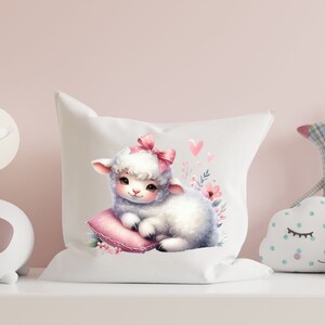 Pu&ograve; includere: Cuscino bianco con un adorabile agnello di cartone animato che indossa un fiocco rosa e giace su un cuscino rosa. L'agnello &egrave; circondato da fiori rosa e cuori.